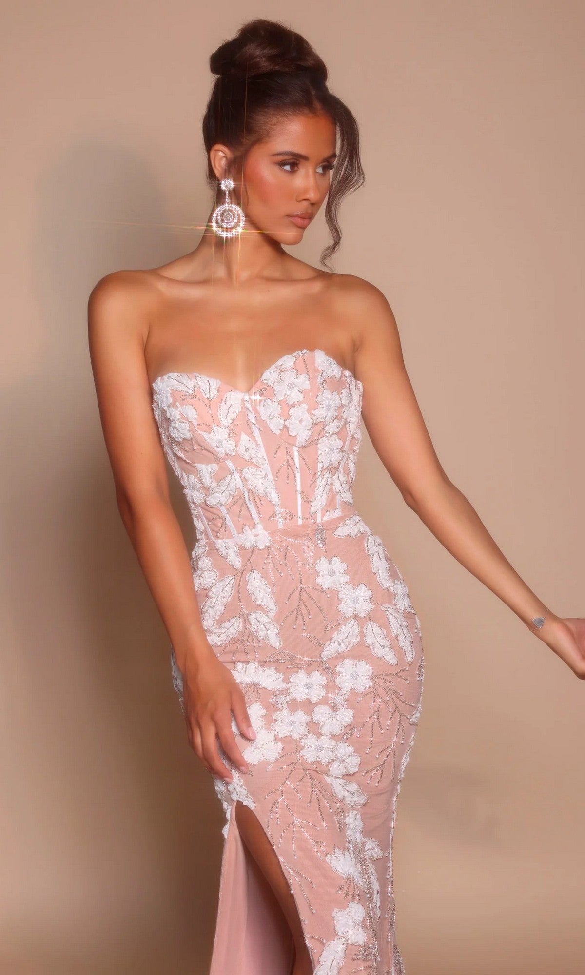Model wearing the Portia and Scarlett PS26074 long formal dress, featuring a strapless sweetheart neckline, light pink floral embroidery, thigh-high slit, and statement earrings against a plain beige background.